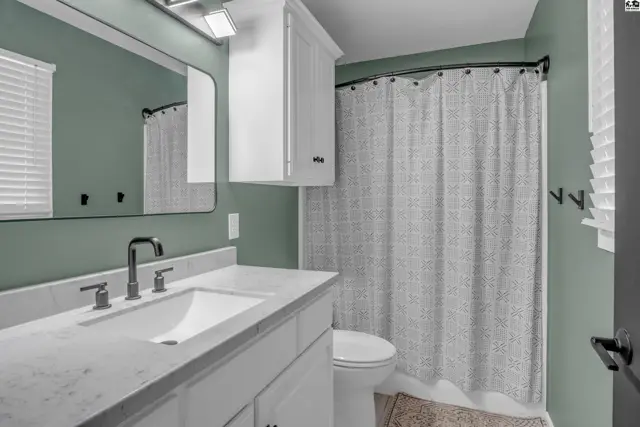 Modern bathroom with a white vanity, quartz countertop, and a patterned shower curtain.