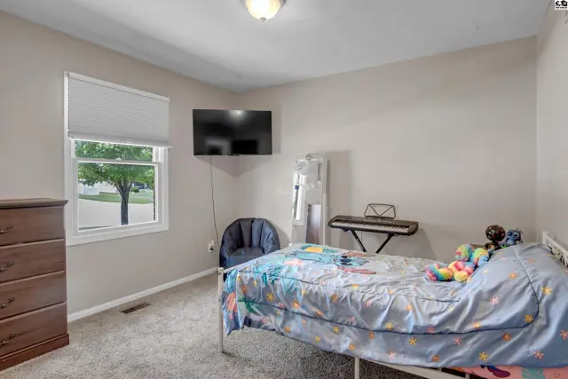 Neutral bedroom with a dresser, bed, keyboard, and wall-mounted TV.
