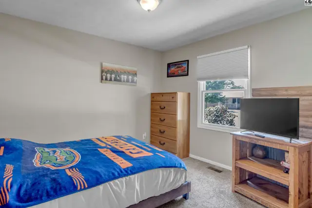 Cozy bedroom with a queen bed, wooden dresser, and TV on a stand.