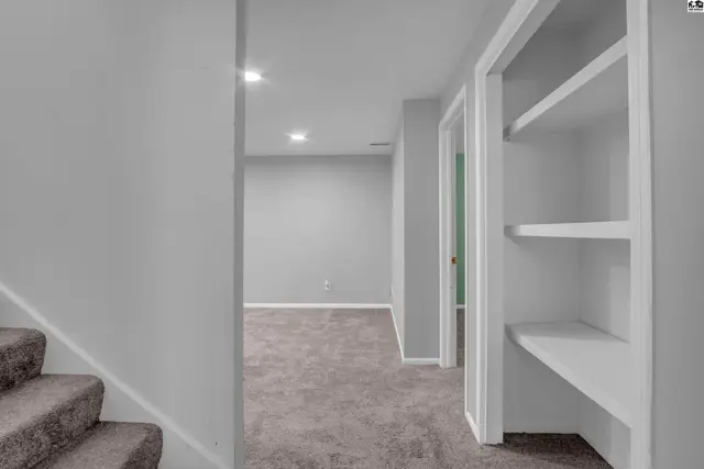 Hallway with gray carpet, white built-in shelves, and a doorway to a room with gray walls.