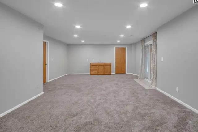 Spacious gray finished basement with plush carpet, wood cabinetry, and sliding glass doors.