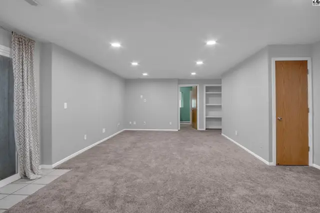 Spacious, light-filled finished basement with plush gray carpet, recessed lighting, and built-in shelving.