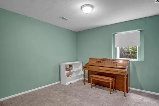 A light-filled room with sage green walls, a brown upright piano, and a white bookshelf.