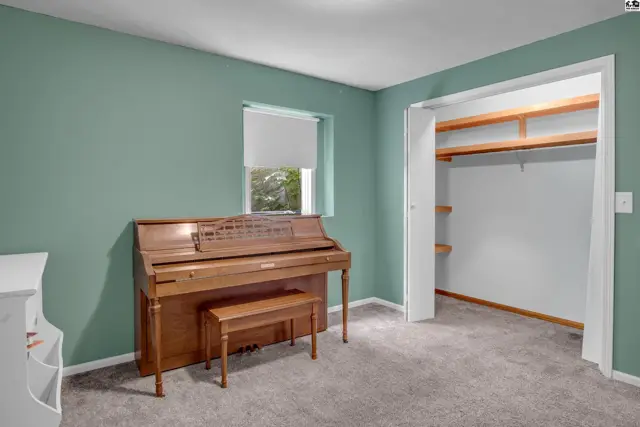 A light-filled room with teal walls, a wooden upright piano, and a spacious closet with open shelving.