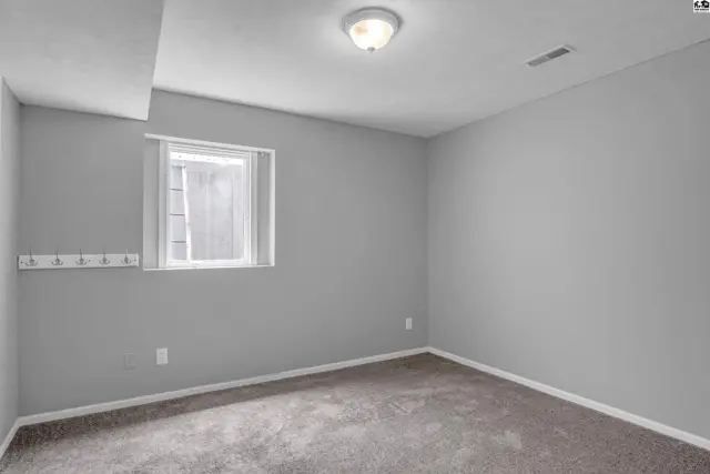 Empty room with gray walls, carpet, and a small window.