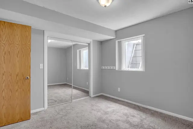 Spacious bedroom with gray walls, carpet, a wooden door, and mirrored closet doors.