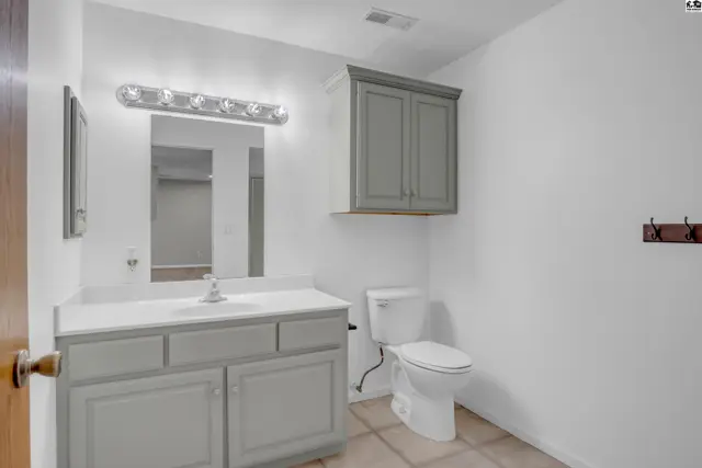 Modern bathroom with gray vanity, white countertop, large mirror, and white toilet.