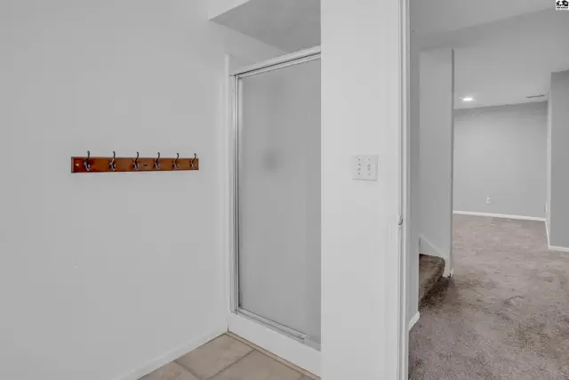 Frosted glass shower stall with a wooden coat rack on a white wall, next to carpeted stairs.