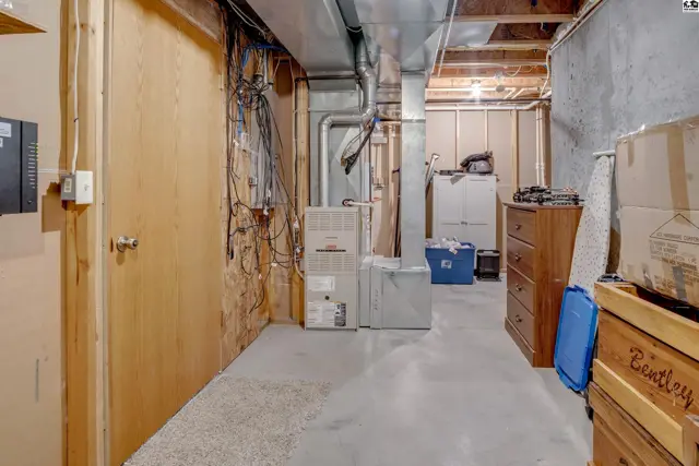 Unfinished basement with concrete floor, exposed joists, furnace, water heater, and wood-paneled door.