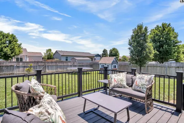 Spacious deck with dark composite flooring, black railing, and outdoor furniture overlooks a green backyard.