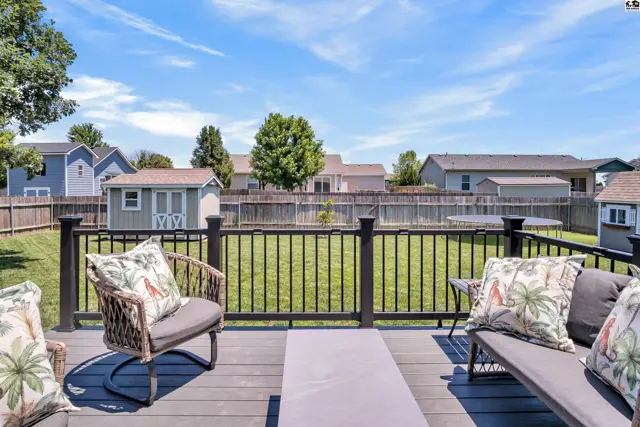 Spacious backyard with a deck, seating, shed, and trampoline under a clear blue sky.