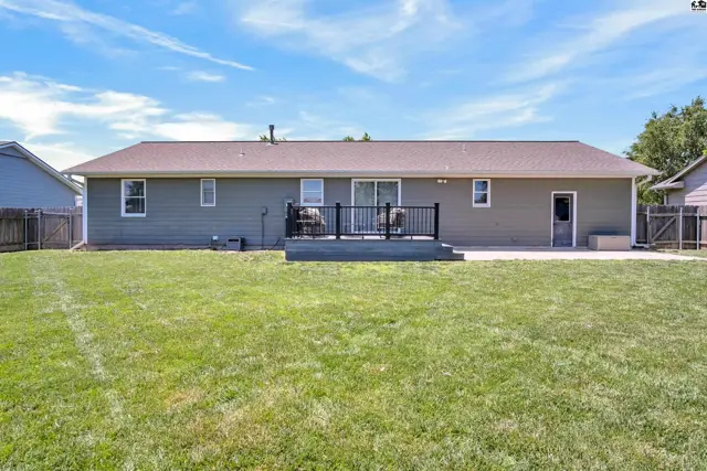 Backyard view of a gray home with a dark deck, patio, and large green lawn.