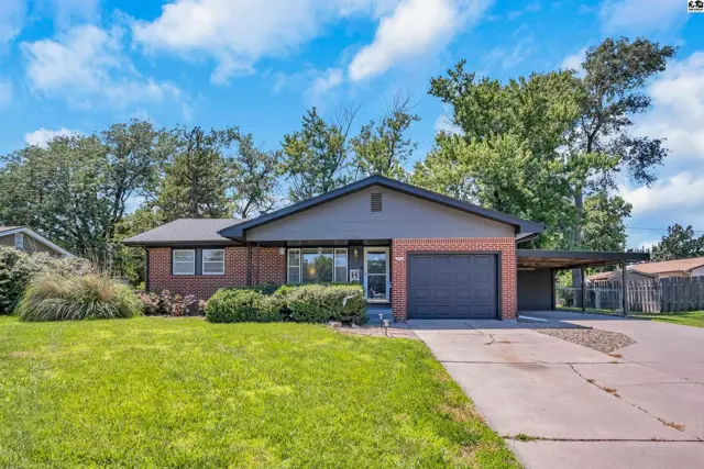 Brick ranch home with a dark gray roof, attached garage, and carport on a sunny day.