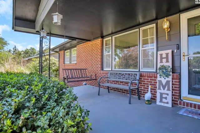 Covered front porch with brick exterior, swing, bench, and "HOME" sign.
