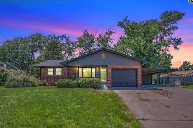 Brick ranch home with a dark roof, attached garage, and covered carport under a colorful twilight sky.