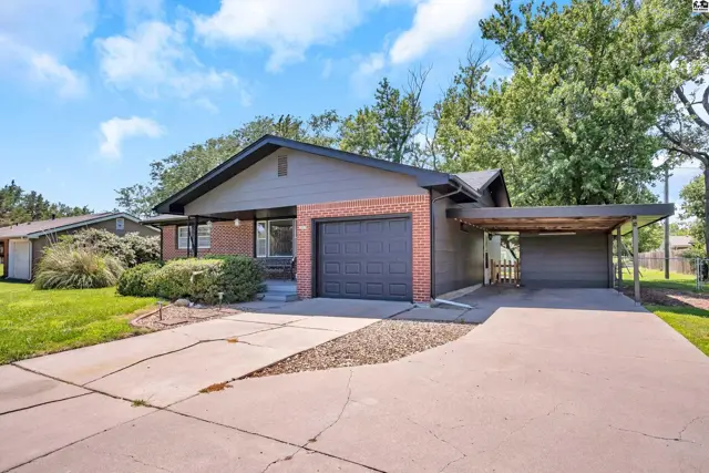 Exterior view of a brick and siding ranch home with a carport and mature trees.