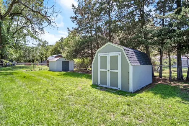 Two backyard sheds, one green with white trim and a gambrel roof, sit on a grassy lawn.
