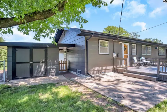 Exterior view of a modern home with a dark gray siding, wooden deck, and attached shed.