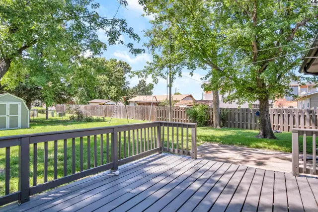 Spacious wooden deck overlooks a fenced backyard with mature trees and a storage shed.