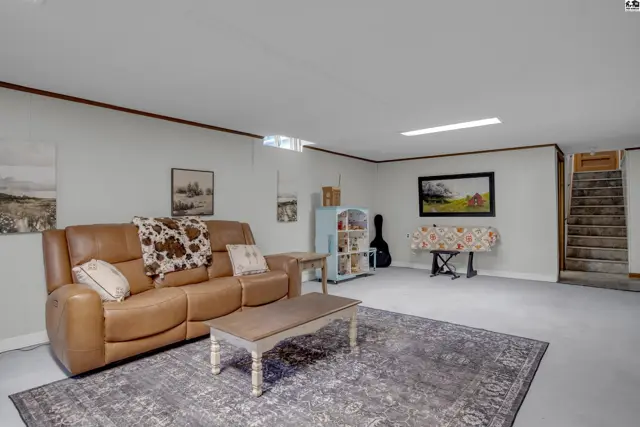 Spacious finished basement with a leather sofa, patterned rug, and stairs leading up.