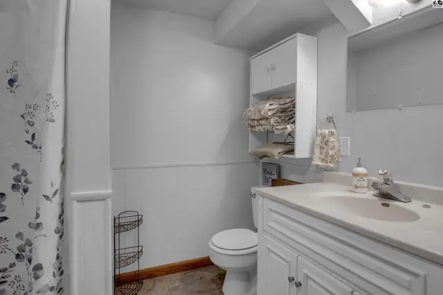 Bright bathroom with white vanity, toilet, shower curtain, and built-in storage cabinet.