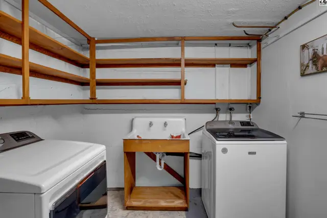 Laundry room with white washer and dryer, utility sink, and ample wooden shelving.