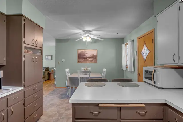 Kitchen and dining area with light green walls, brown cabinets, and a white countertop.