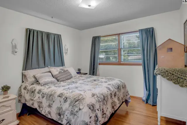 Bedroom with a floral comforter, wood floors, and large windows framed by blue curtains.