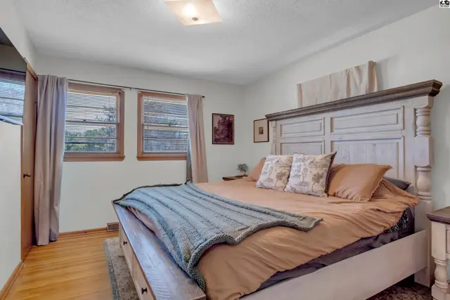 Spacious bedroom with a large distressed wood headboard, neutral bedding, and hardwood floors.