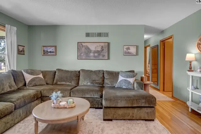 Spacious living room with a large sectional sofa, light wood floors, and pale green walls.