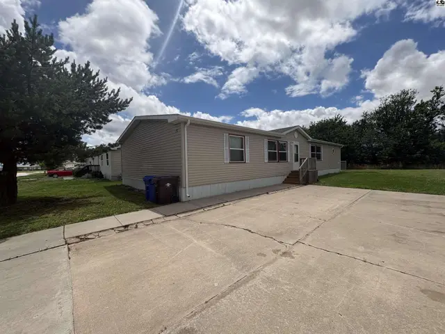 Manufactured home with beige siding, white trim, and a concrete driveway under a cloudy sky.