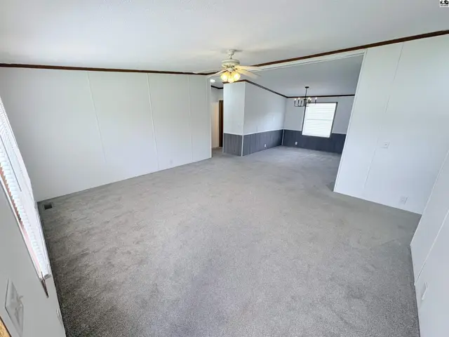 Spacious living room with neutral carpet, white paneled walls, and a gray accent wall.