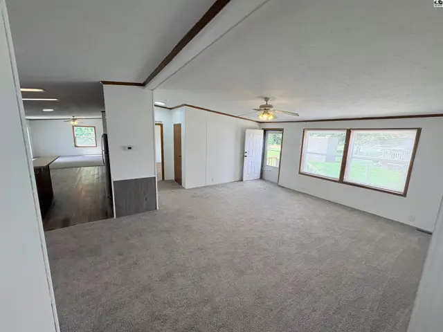 Spacious living room with plush carpet, white walls, and large windows opening to a deck.