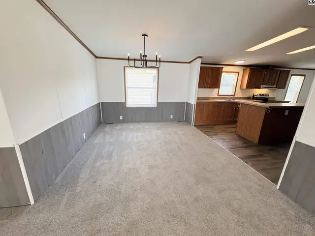 Spacious living and dining area with gray wainscoting and plush carpet, opening to a modern kitchen.