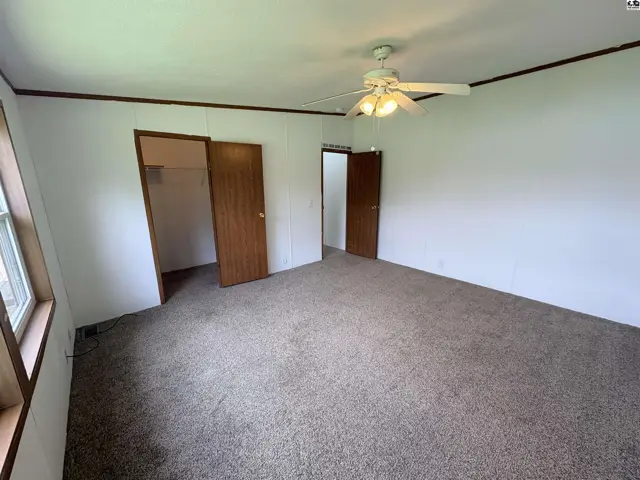 Spacious bedroom with plush carpet, wood doors, and a ceiling fan.