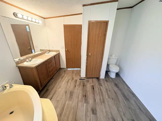 Spacious bathroom with double vanity, wood cabinets, light wood-look flooring, and a separate toilet area.