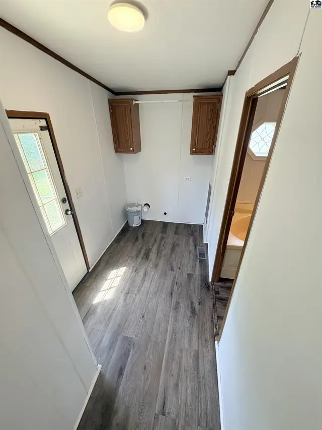 Laundry room with wood-look vinyl flooring, white walls, and dark wood cabinets.