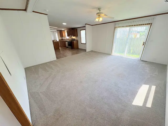 Spacious living room with plush carpet opens to a kitchen with wood cabinets and sliding glass door.