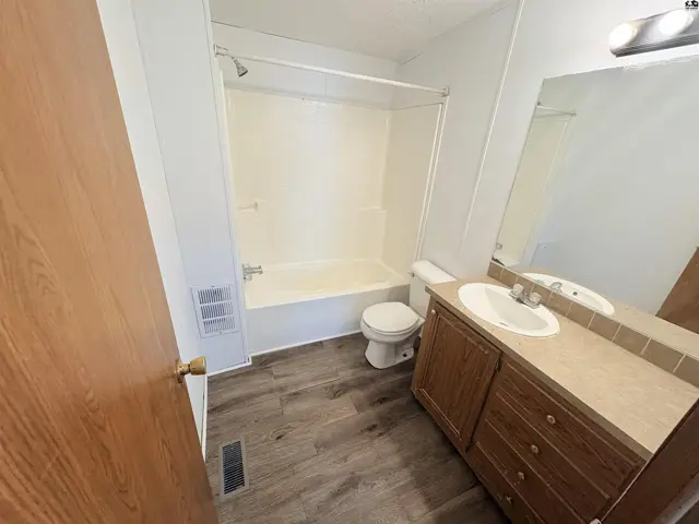 Bright bathroom with a white tub/shower, vanity, and wood-look flooring.