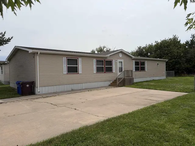 Tan vinyl-sided manufactured home with white trim and a concrete driveway.