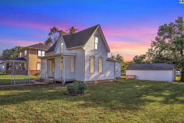 Charming white Victorian-style house with a porch and detached garage under a colorful sunset sky.