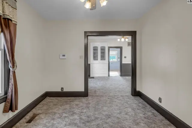 Living room with plush gray carpet, dark trim, and a doorway to a bright kitchen.