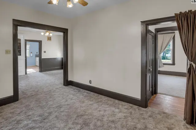 Living room with plush gray carpet, dark wood trim, and doorways to other rooms.