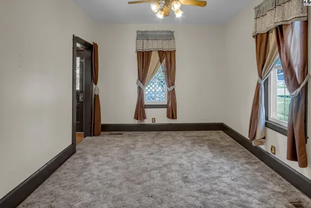 Spacious living room with plush carpet, dark trim, and decorative curtains on two windows.