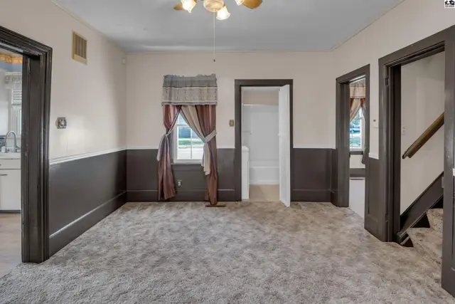 Spacious living room with plush carpet, dark wainscoting, and doorways leading to other rooms.