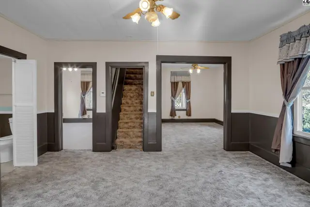 Spacious living room with plush carpeting, dark wood trim, and doorways leading to a staircase and another room.