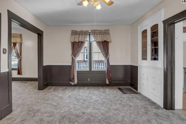 Spacious living room with plush carpet, dark wainscoting, and a built-in white cabinet.