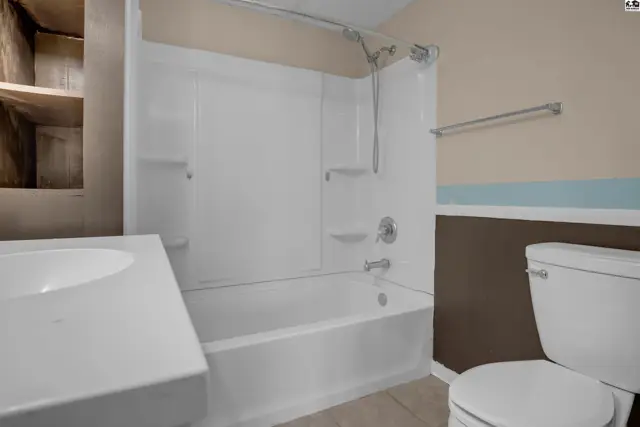 Modern bathroom with white tub, shower, vanity, and toilet against beige and brown walls.