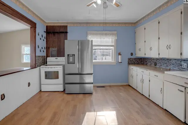 Bright kitchen with light wood floors, white cabinets, stainless steel appliances, and blue patterned wallpaper.