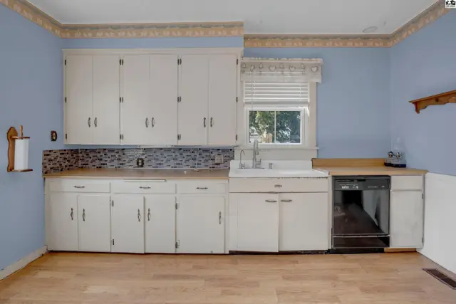 Bright kitchen with white cabinets, wood countertops, mosaic tile backsplash, and light wood flooring.